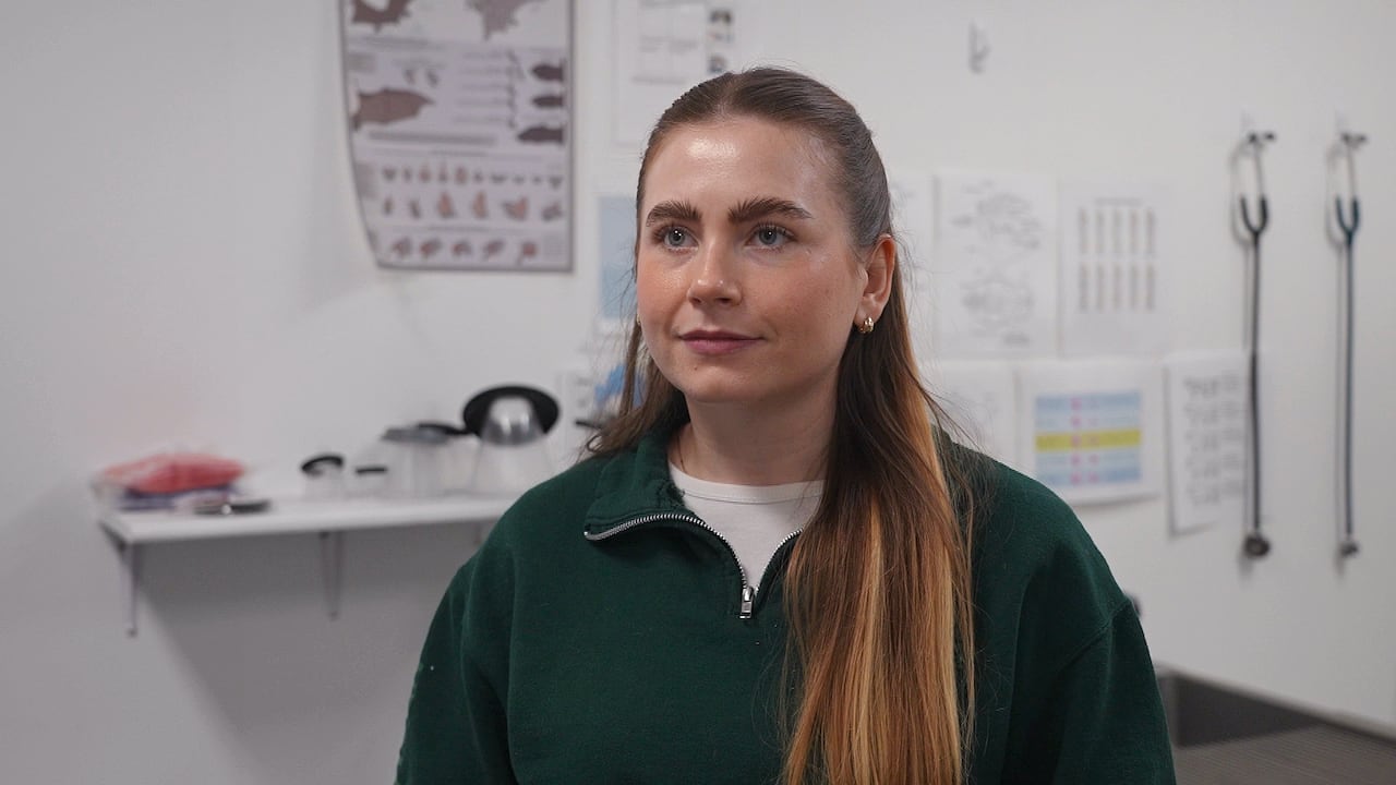 A woman smiles at the camera with veterinary charts in the background.