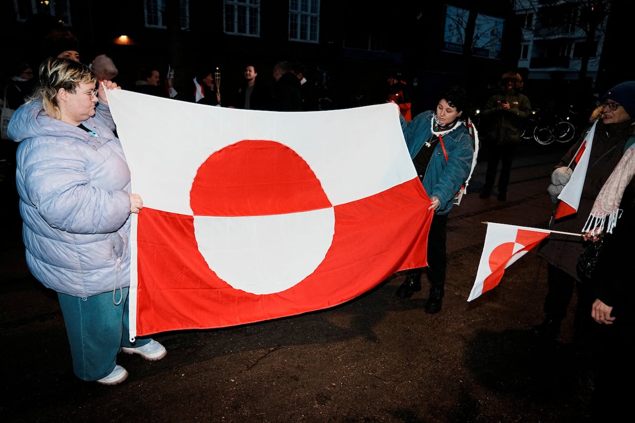 Demonstrators hold up a large Greenland flag