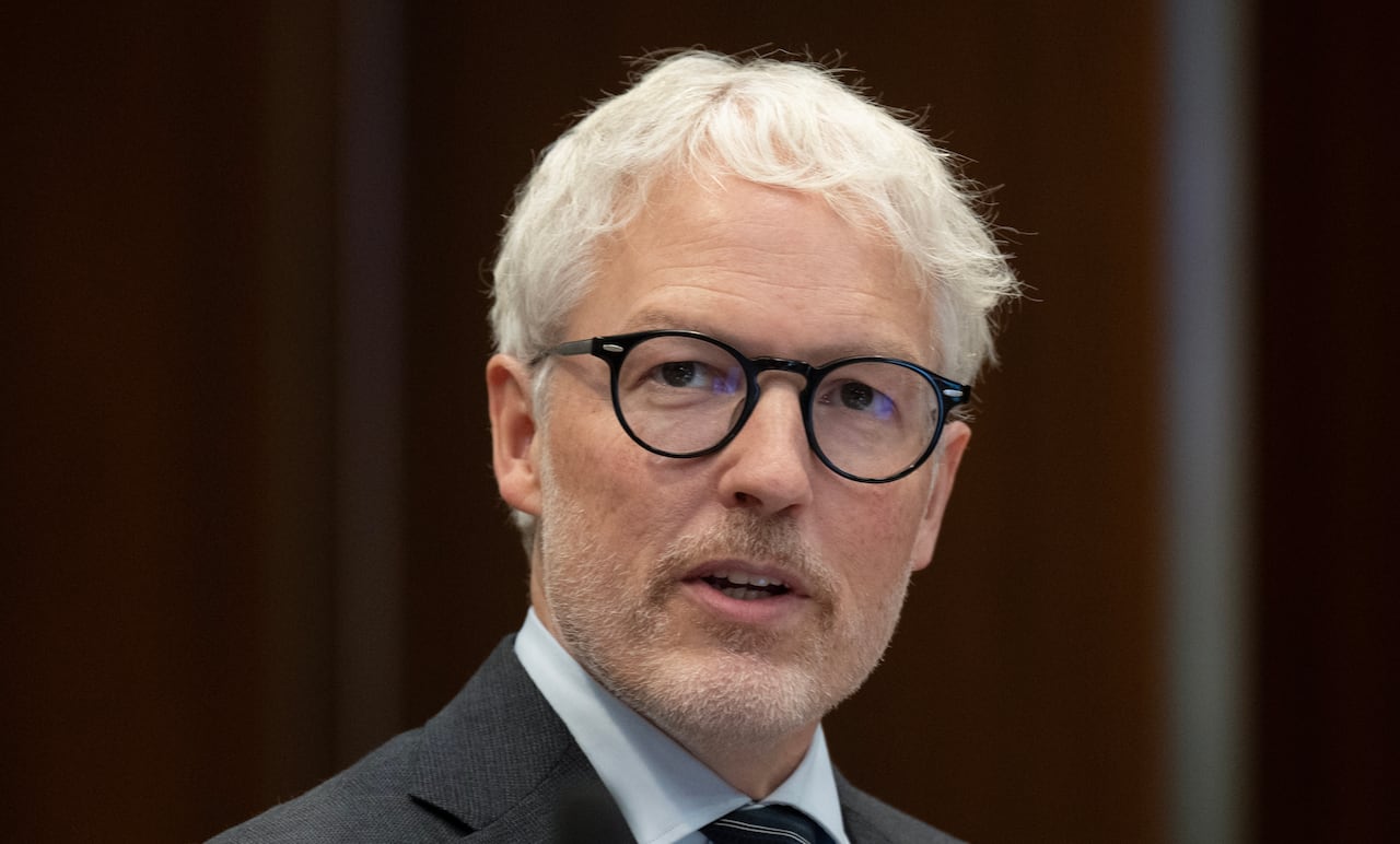 A photo of a man in dark-rimmed glasses, with white hair.
