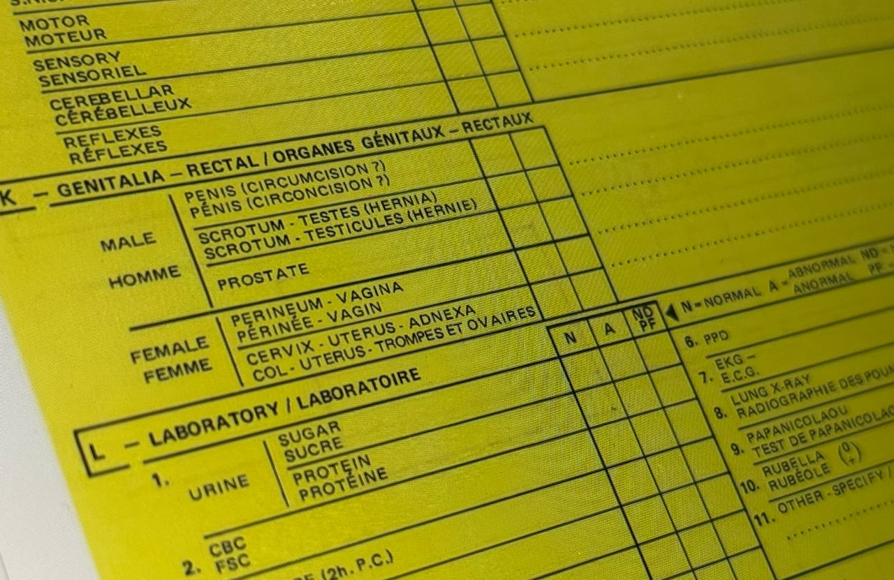 A close up of a yellow form that outlines RCMP's medical exams. A portion lists male and female genitalia with check mark boxes beside each one. 