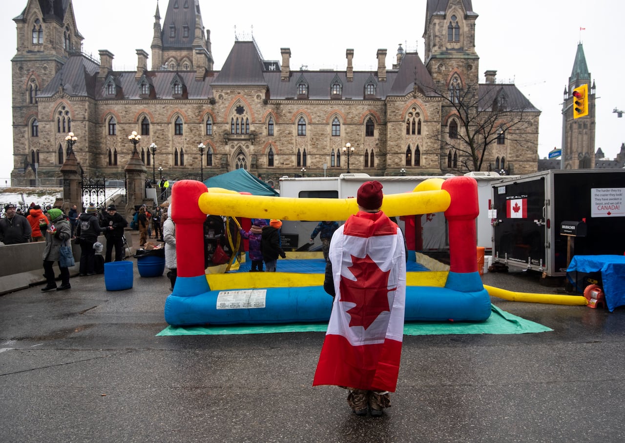 A protester wearing a Canadian flag takes a photo of children playing on a bouncy castle 