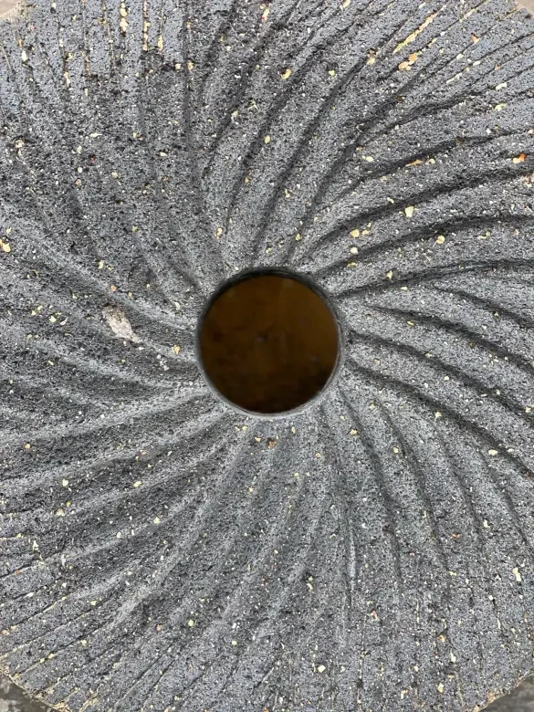 A volcanic rock with striations and a circle hole in the center.