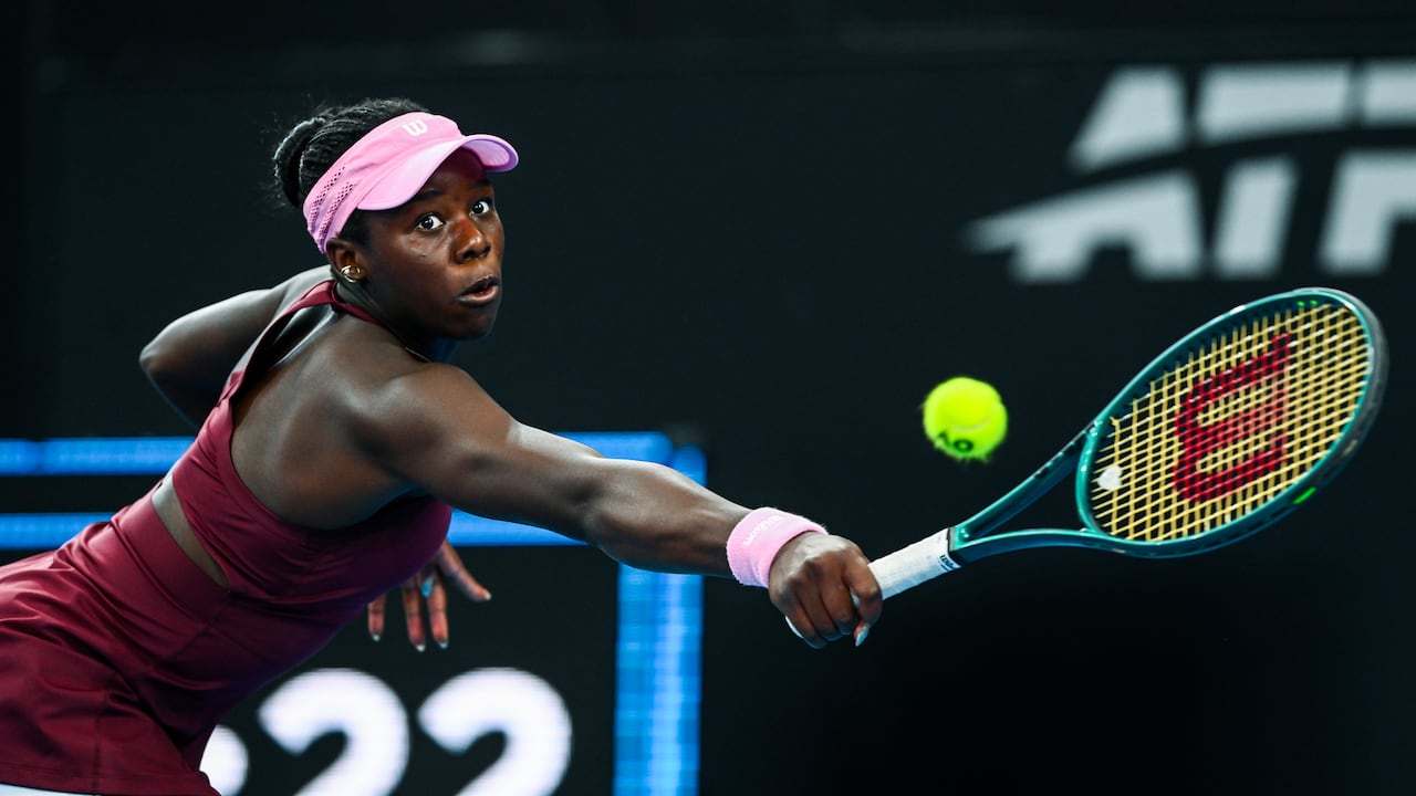 A women's tennis player is shown reaching to make a shot.