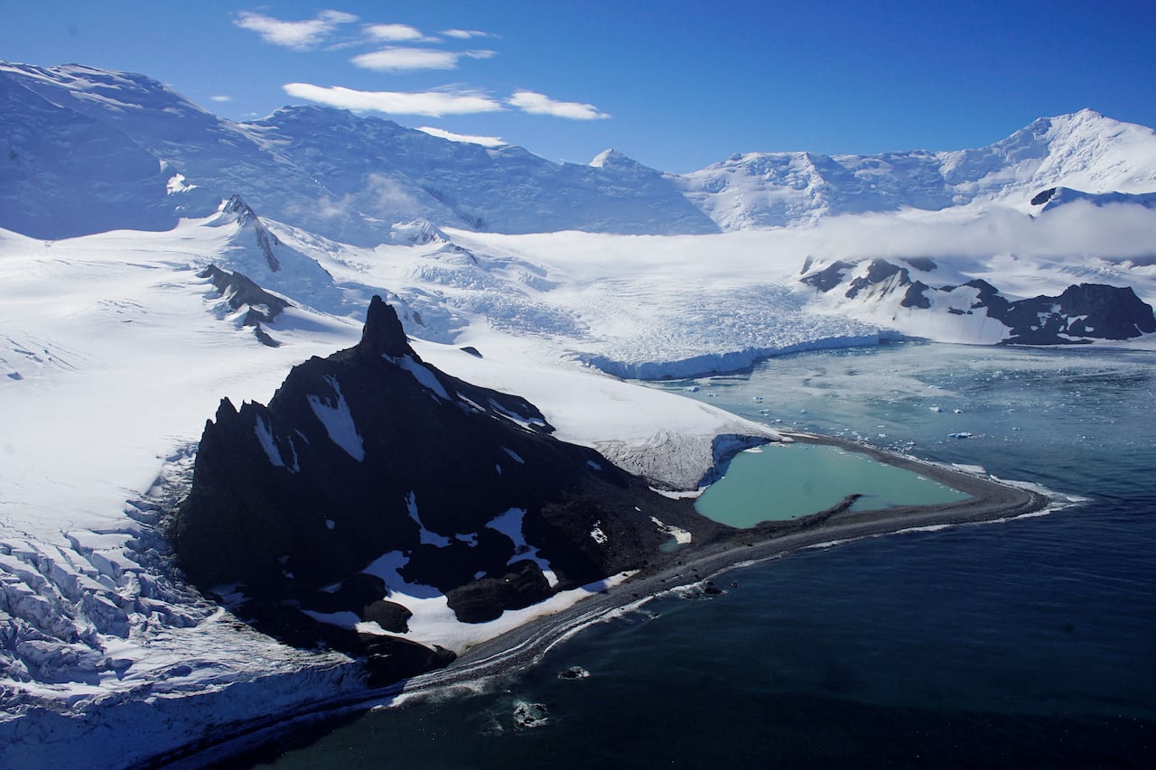 landscape photo of snow covered mountains, a glacier and a large body of water on a sunny day.