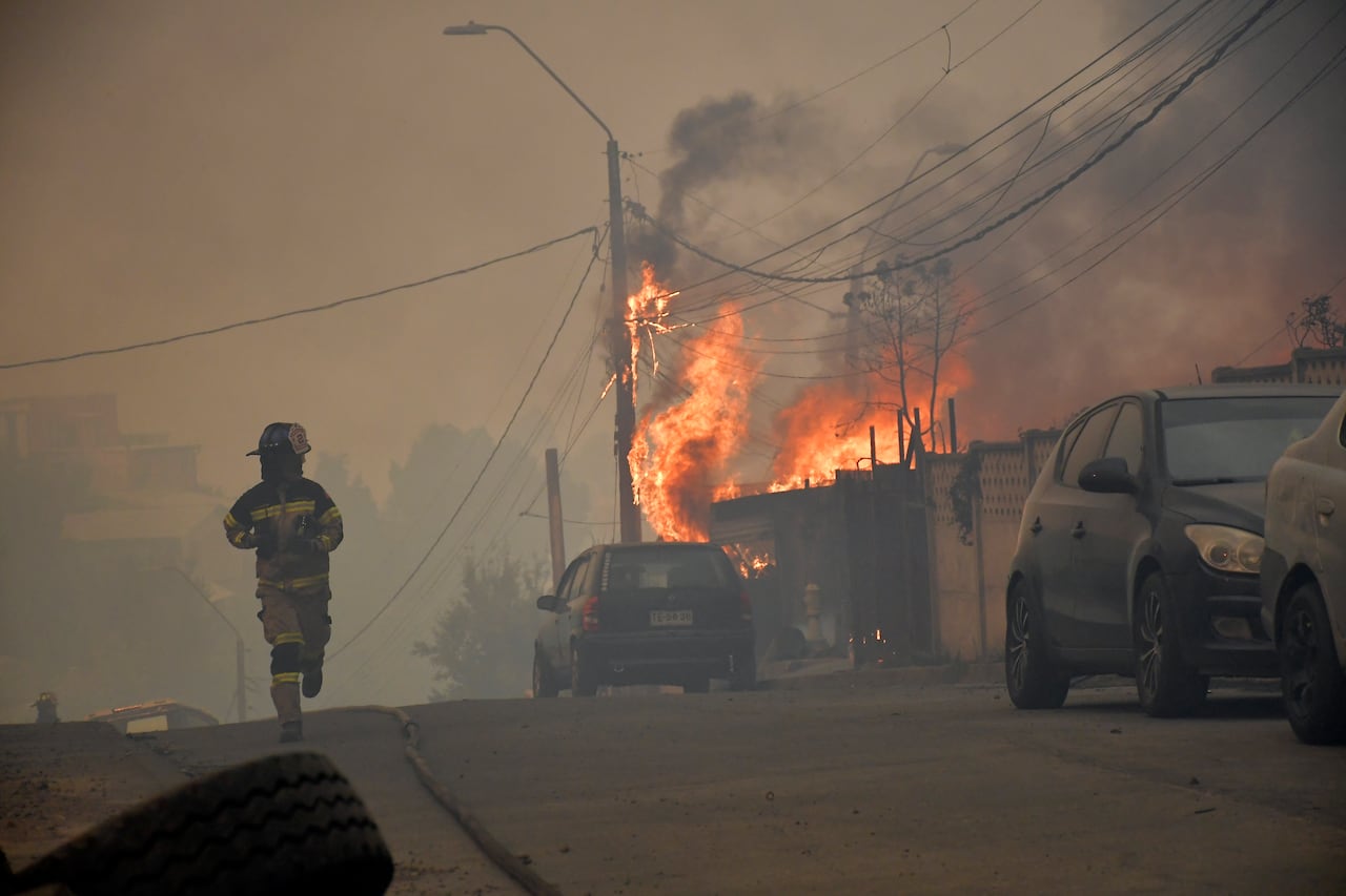 A firefighter runs along a street as a house burns.