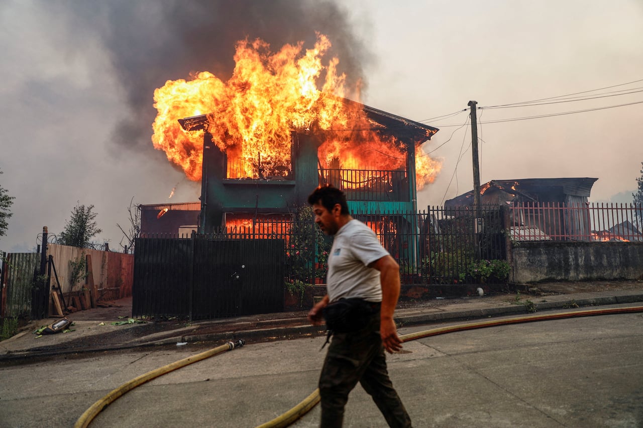 A person walks past a burning home.