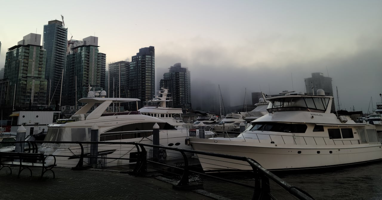 A series of skyscrapers and boats are seen with fog all around.