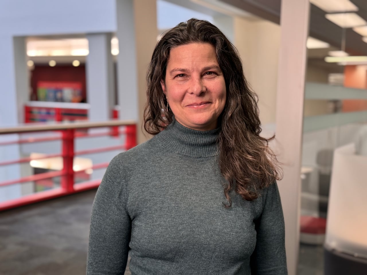 A woman with long brown hair and a grey sweater smiles at the camera