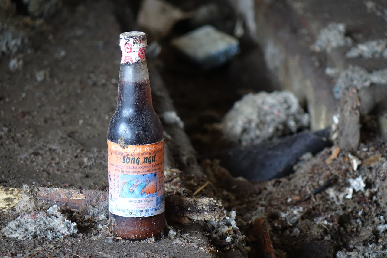 A dirty bottle of long expired fish sauce sits on the ground of a fish plant.