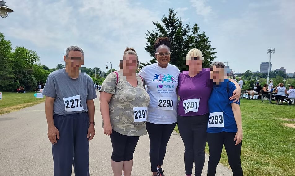 Five people wearing race bibs pose outside. All but one have their faces blurred.