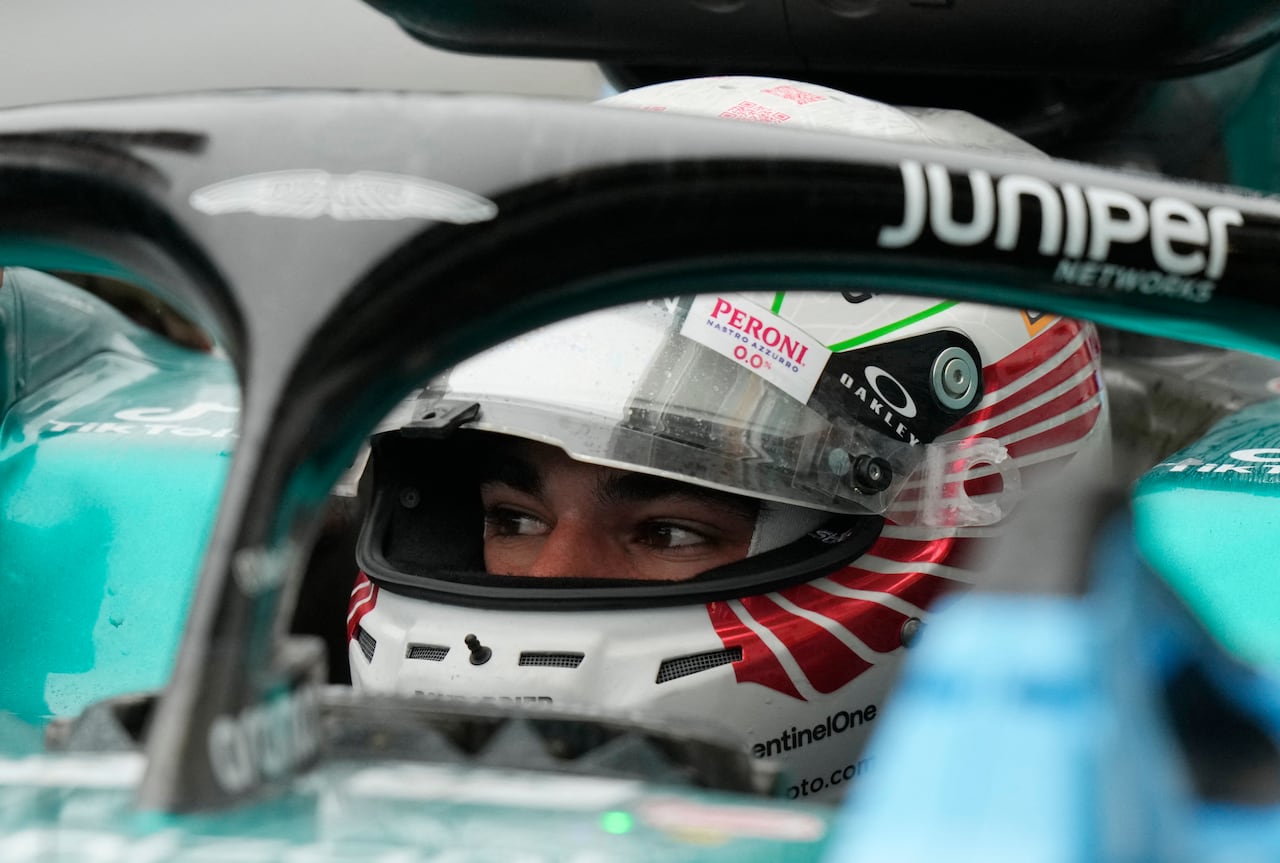 The eyes of a race car driver are seen under his helmet, the photo is taken through the body of the car.