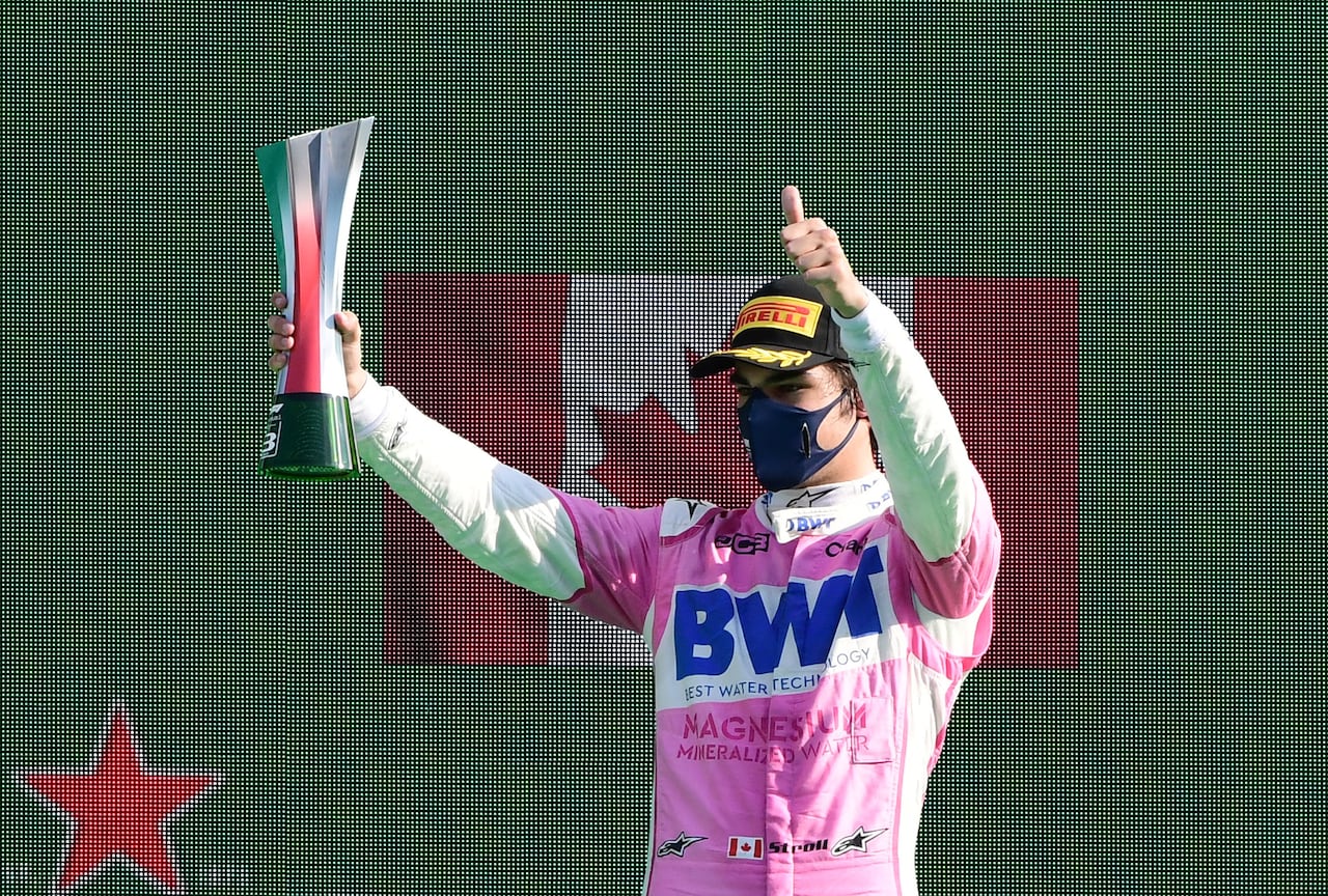 A man wears a face mask and baseball cap. He's holding a trophy and a Canada flag is in the background.