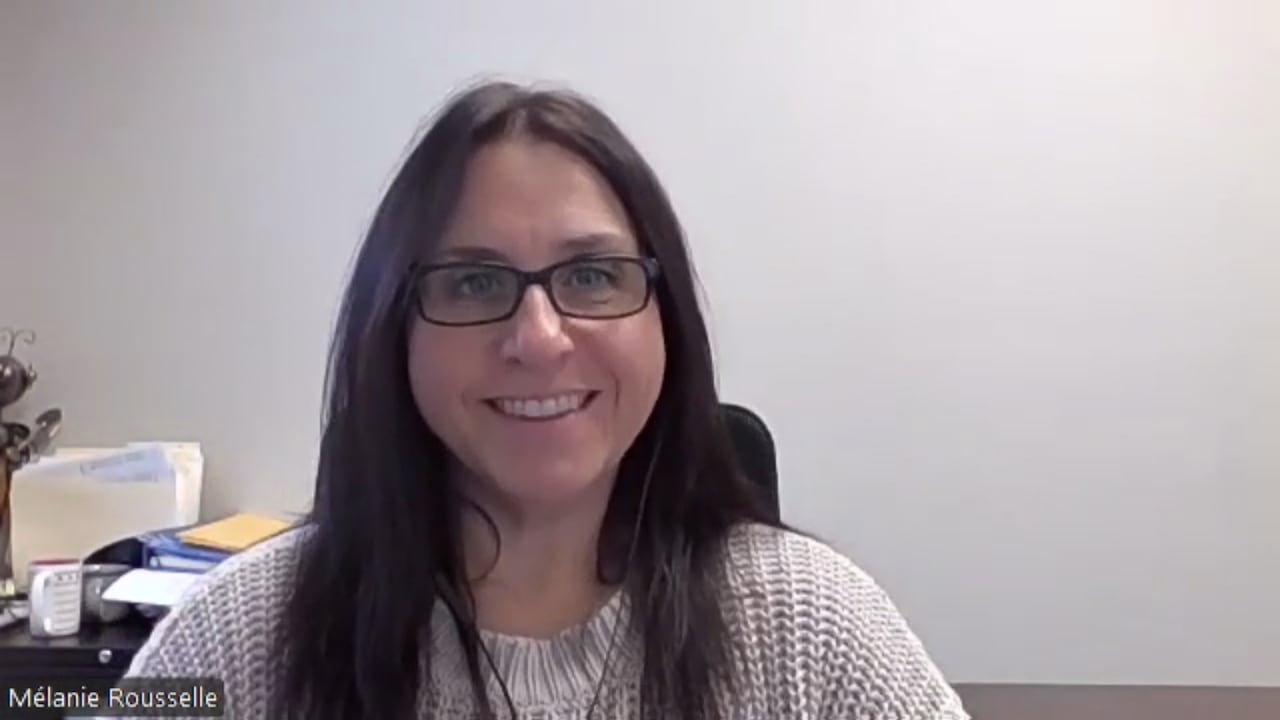 A woman with long brown hair and wearing a white sweater, smiling.