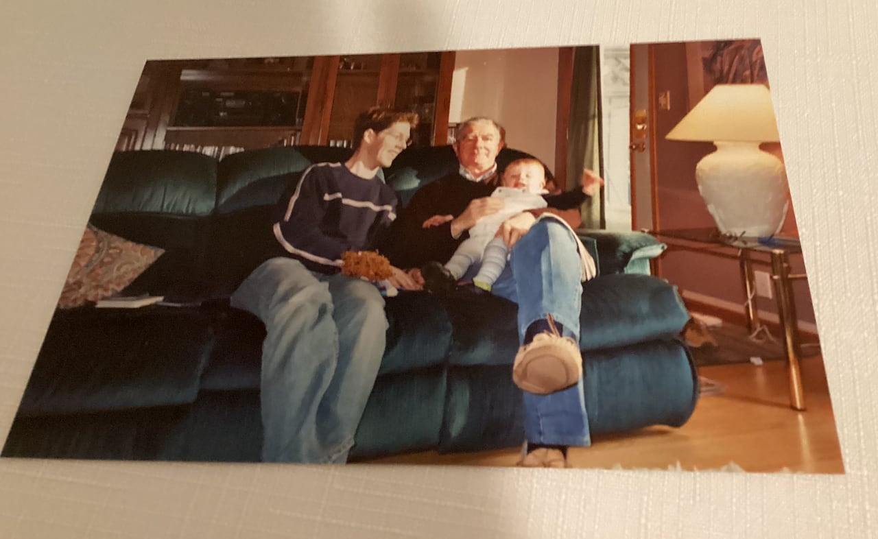 A picture of an old man holding a baby, while another youth next to him laughs.