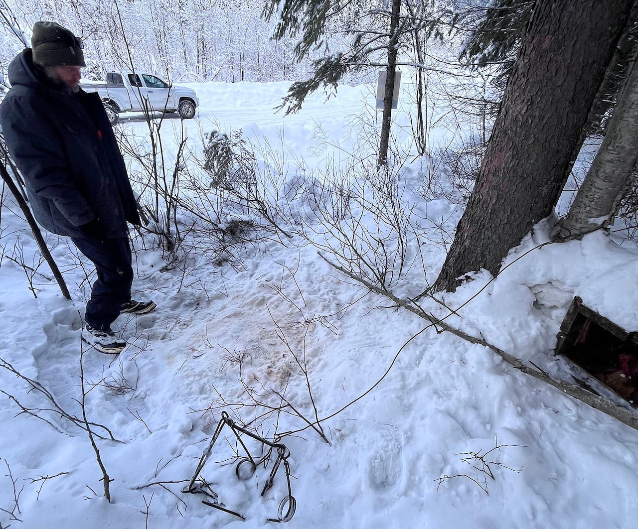 A man stands in the snow, with a truck in the background. 