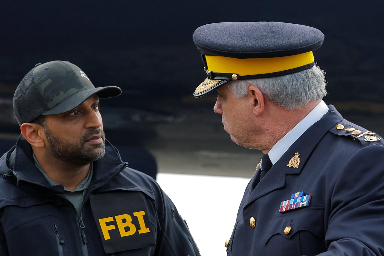 A man in a ball cap and an FBI jacket speaks to a man in a blue RCMP uniform.