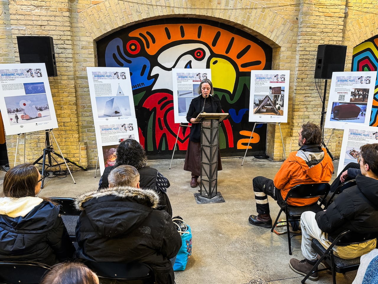 A woman speaks into a microphone mounted to a lectern in front of a series of posters at an announcement.