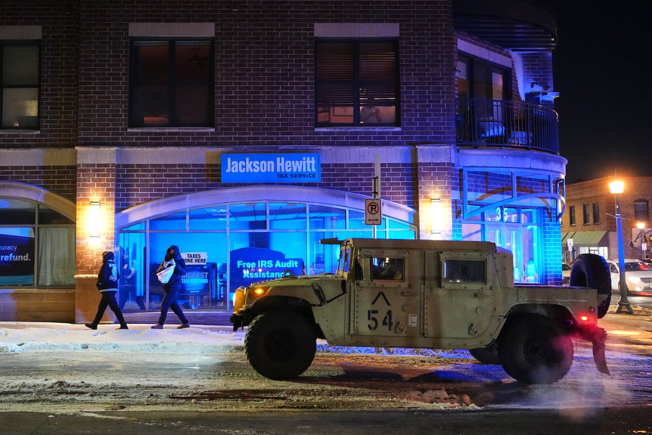 A large military jeep sits in front of a commercial building on a city street at night.