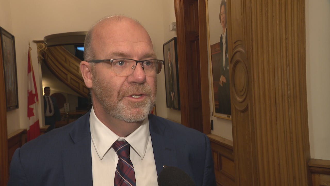 Man in dark blue suit stands in front of hallway with Canadian flag behind.