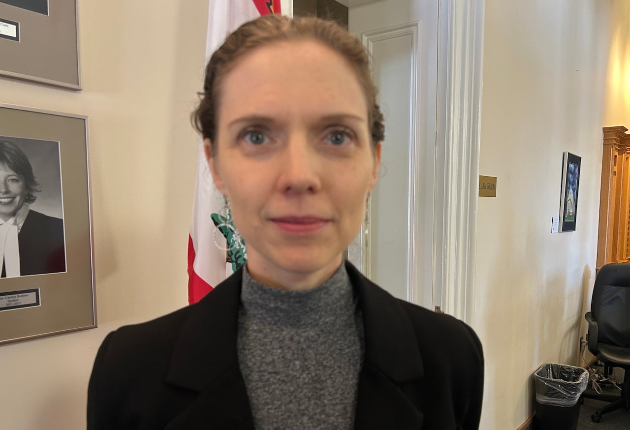 Woman wears grey turtle neck and black blazer and looks at camera