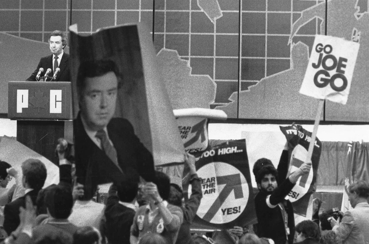 A black and white photo shows a man speaking at a podium to a crowd holding signs.