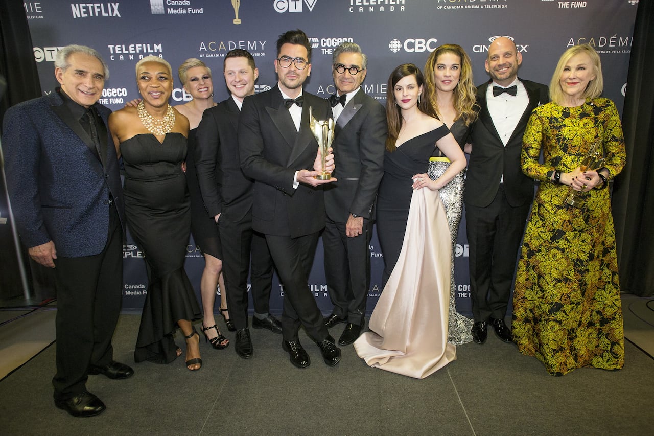 A group of people dressed in fancy clothes stand for a photo, with man front and centre holding an award. 