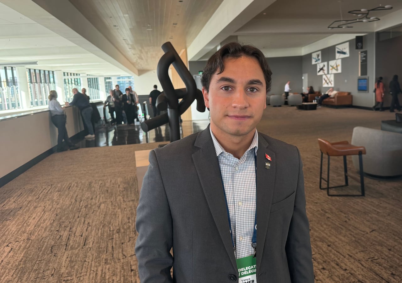 A young man stands wearing a suit jacket.