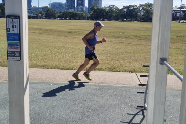 A jogger running outside next to a field.