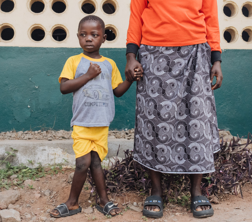 boy in yellow and grey tshirt holds a woman's hand. his knees are bent together