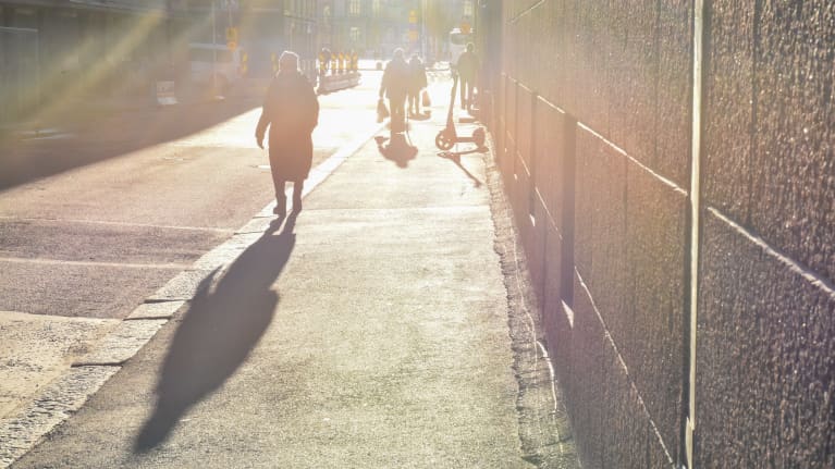 A few people walking on a city sidewalk in a photo drenched in hazy golden sunlight.