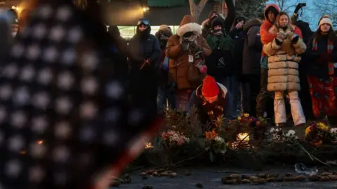 Reuters People lay flowers, candles and pine cones in a street. An American flag can be seen in the front of the picture