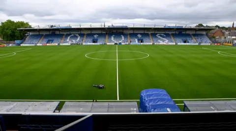 SNS A view of Queen of the South's Palmerston Park with a synthetic playing surface and a stand with the letters QOS in white on a blue background