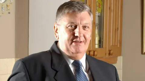 BBC The actor Derek Martin wears a suit and tie.