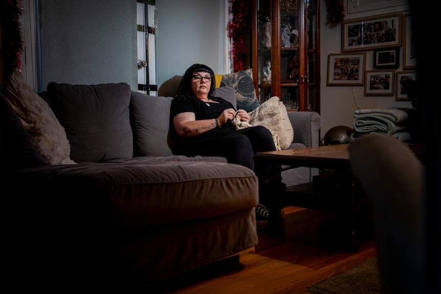 LJ sits on a couch knitting