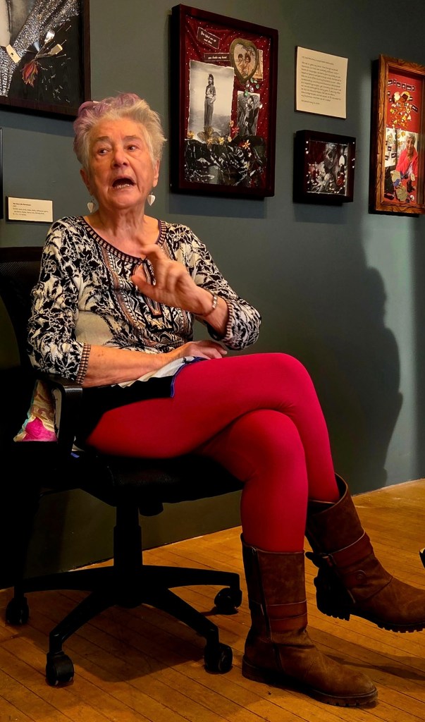 older woman in red tights, seated, speaking in art gallery