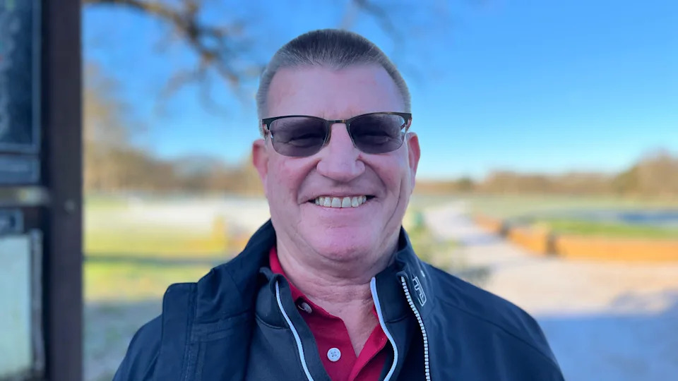 Alan Covey, a middle-aged man with short hair, wears sunglasses and a blue jacket over a red polo shirt, as he smiles into the camera.