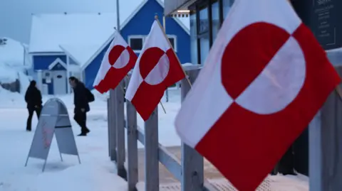 AFP via Getty Images  People walk past Greenlandic flags outside a shop in the city centre