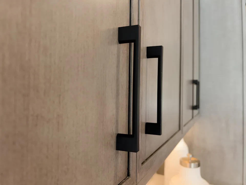 Close-up of a wooden cabinet with sleek, modern black handles. A decorative bottle is partially visible on the countertop below
