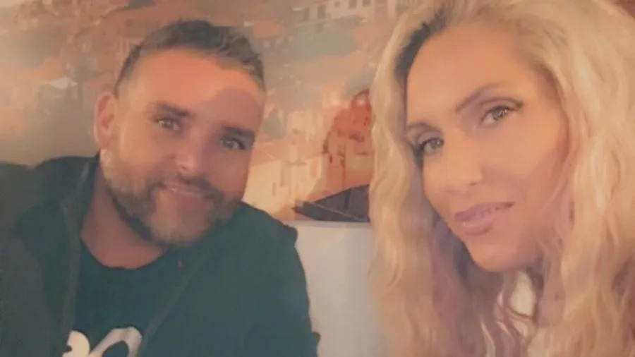 Jessica, who has long blonde hair, smiles in a selfie with her husband Dan, who is wearing a black jumper and has short silvery hair and stubble.