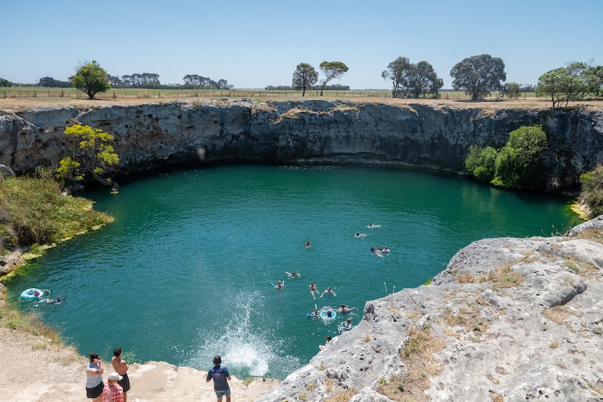 A swimming lake, surrounded by a circle of rocky cliffs, with swimmers in the lake