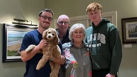 Darren Kidd/BHF A bald man, wearing glasses, standing in between two men and a woman. The man on the left is holding a dog. 