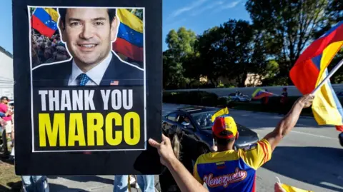 EPA/Shutterstock Venezuelans in Miami, Florida, hold a picture of US Secretary of State Marco Rubio during a rally in support of the US operation in Venezuela. Photo: 3 January 2026