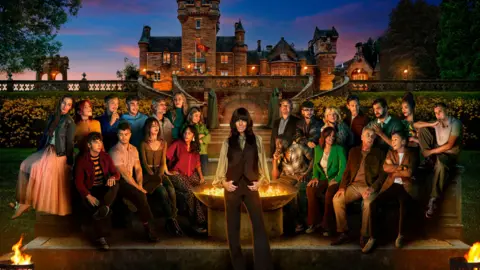 BBC/PA An image of the cast of Series 4 of The Traitors. (left to right back row) Rachel, Jessie, Stephen, Faraaz, Maz, Ellie, Harriet, Hugo, Jack, Fiona, Sam, Adam, Roxy, Reece, (left to right front row) James, Matthew, Jade, Netty, Ross, Judy, Ben, Amanda and host Claudia Winkleman (standing centre). The cast are all stood or seated in front of the iconic Scottish castle where the show is filmed. Claudia is in front of a fire pit. 