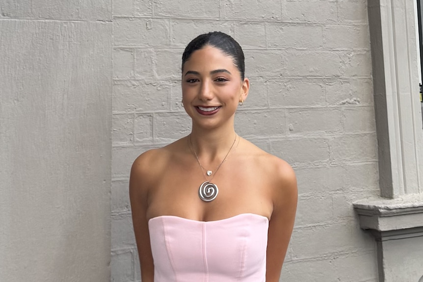 A girl with a dark ponytail in a pale pink top.