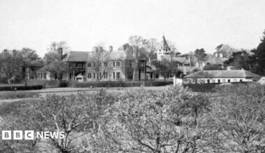 A black and white image of the hospital from the distance. A Victorian looking building can be seen from behind some bushes.