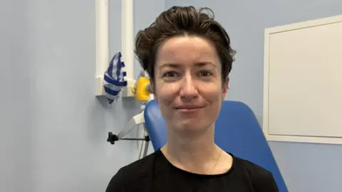 NHS Sussex Dr Aoife Fordham, an urgent treatment centre doctor in a NHS clinical room wearing a black T shirt.