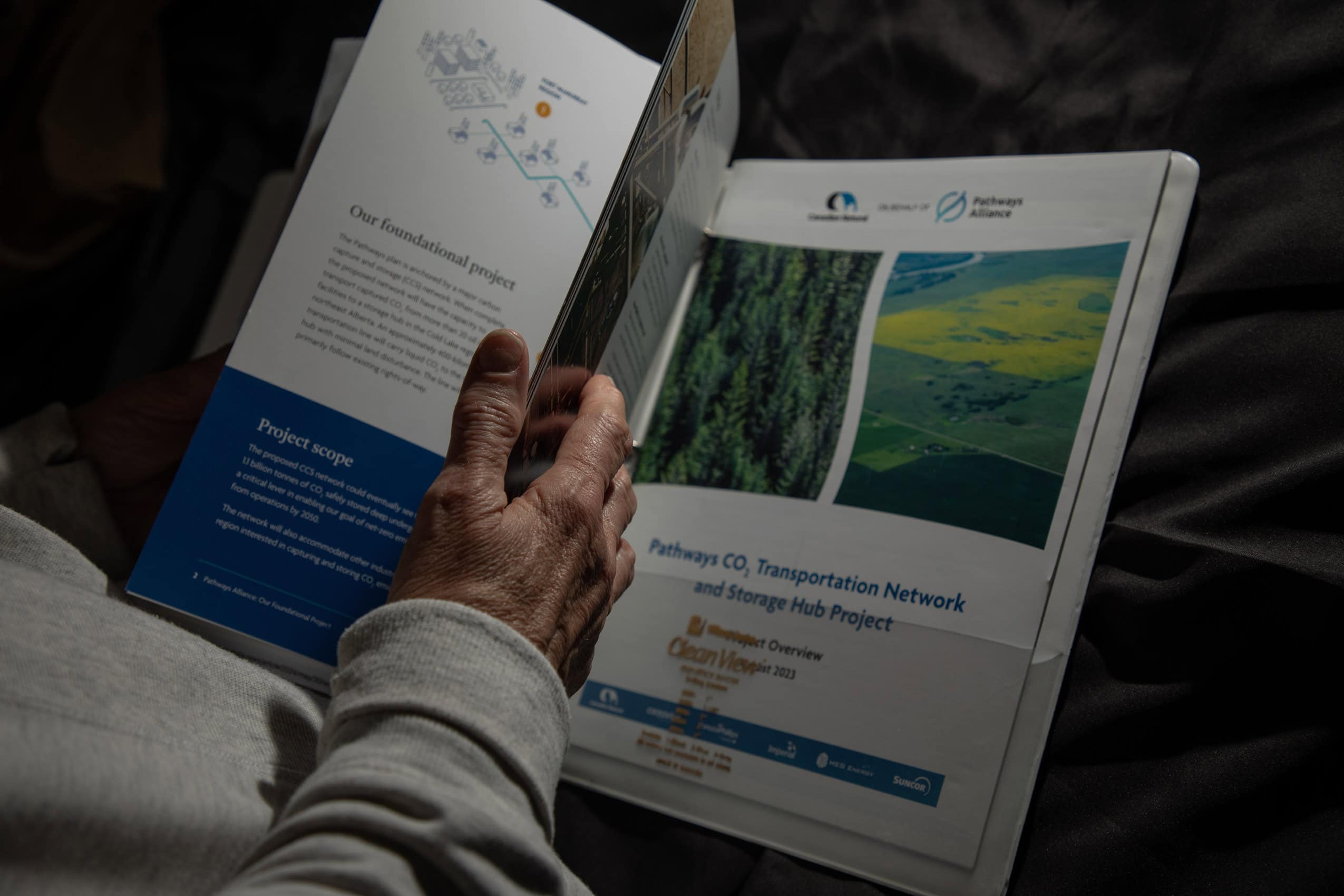 A person's hand flips through a binder with papers about the Pathways Alliances carbon dioxide transportation network and storage hub project.