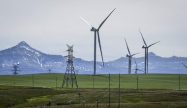 Wind turbines and power transmission lines are seen near Pincher Creek, Alta., with mountains in the background.