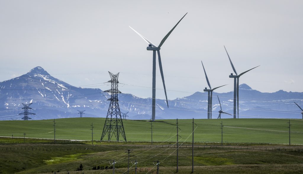 Wind turbines and power transmission lines are seen near Pincher Creek, Alta., with mountains in the background.