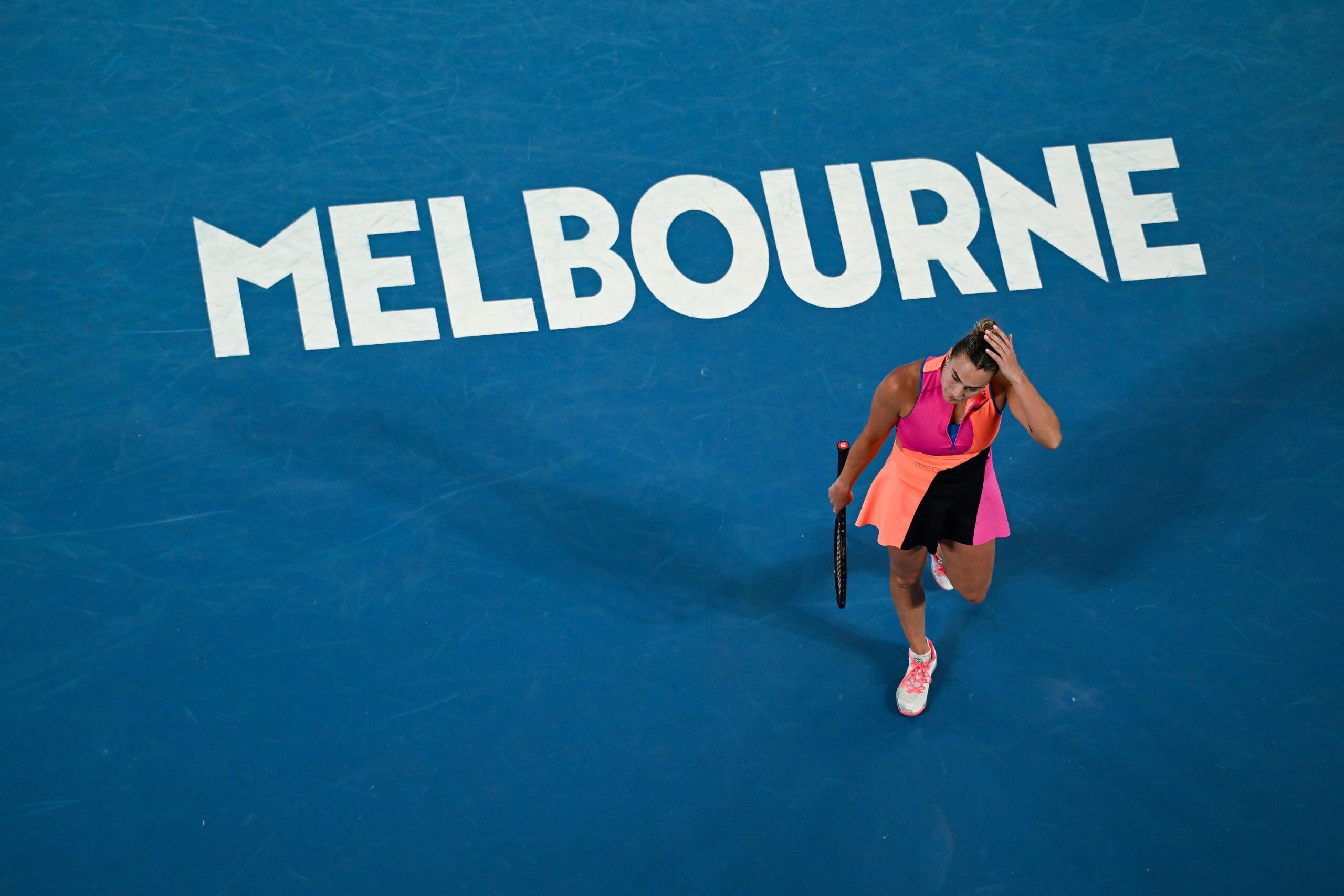 Aryna Sabalenka scratches her head in bird's-eye view on a blue tennis court with the word "MELBOURNE" in all-white capital letters.